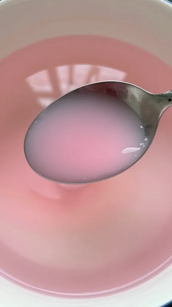 closeup of a single spoon stirring pink dye into clear water